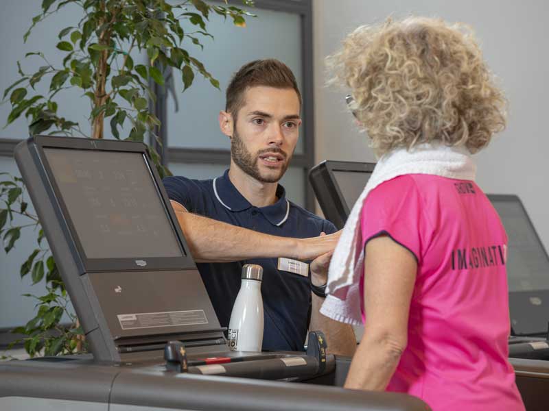 Donna cammina in palestra. Fa esercizio di equilibrio e fiato. Un personal trainer la affianca 