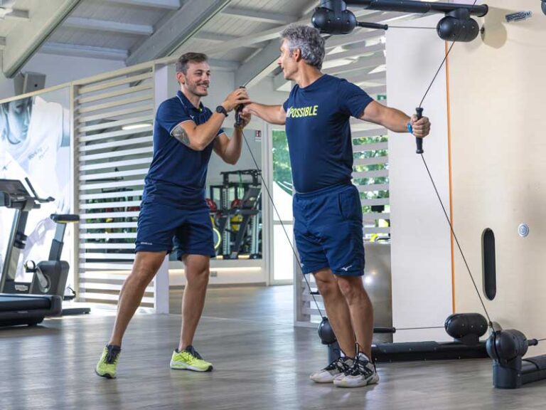 Personal trainer prende in mano il manubrio del Kinesis e guida l’atleta durante l’allenamento in palestra.