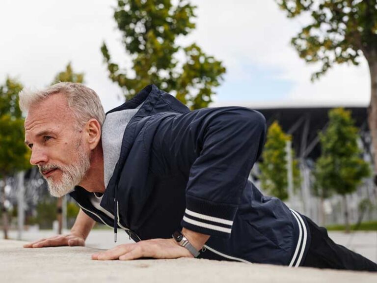 uomo si allena al parco, sta facendo un allenamento metabolico e sta eseguendo l'esercizio push-up su un muretto