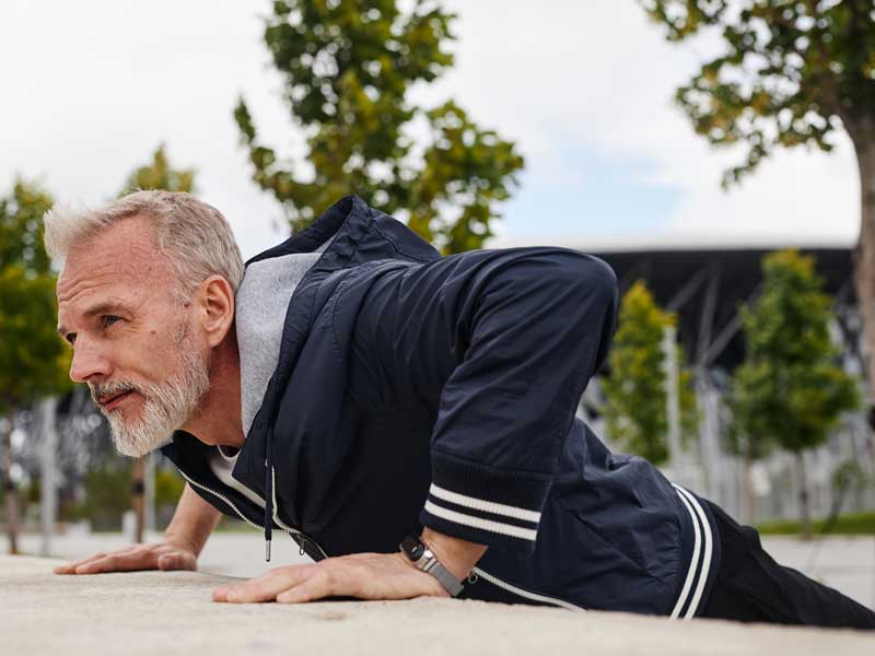 uomo si allena al parco, sta facendo un allenamento metabolico e sta eseguendo l'esercizio push-up su un muretto