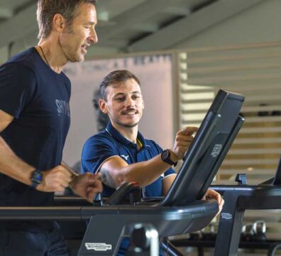 uomo corre sopra il tapis roulant seguito dal personal trainer per un allenamento di fiato