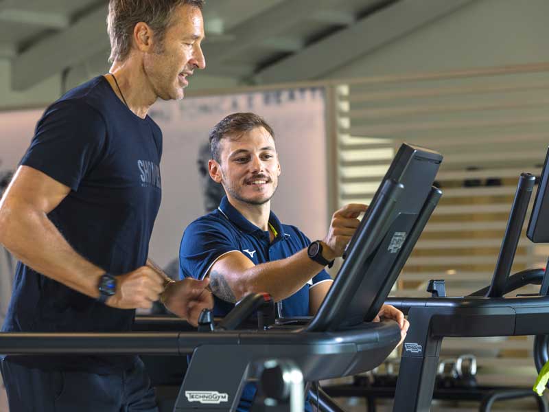 uomo corre sopra il tapis roulant seguito dal personal trainer per un allenamento di fiato
