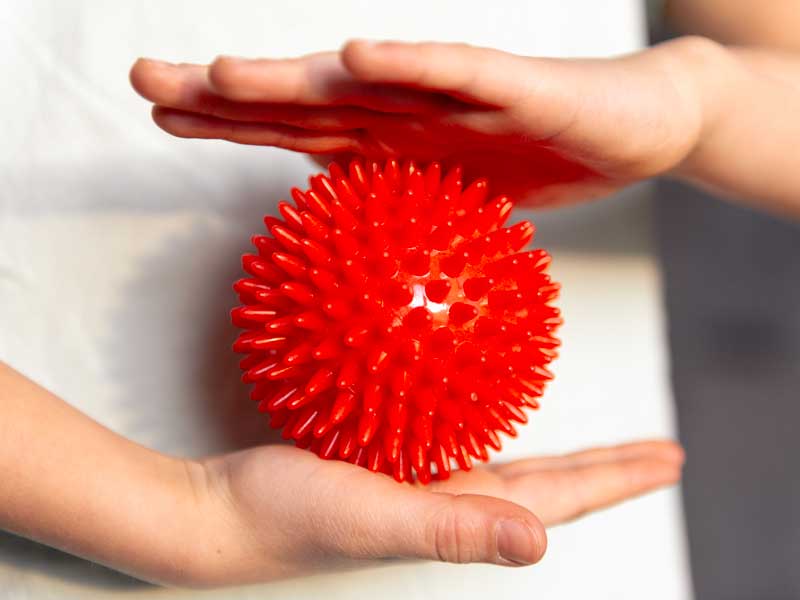 mani tengono una Sensyball che è una pallina in plastica con punte morbide per il massaggio del corpo