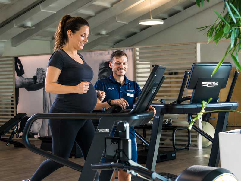 donna cammina su un tapis roulant in palestra seguita da un personal trainer