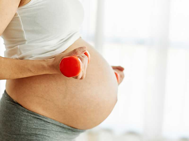 donna in cinta con pesi in mano si allena