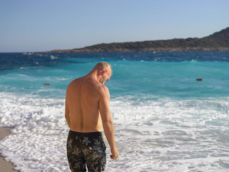 Uomo di spalle sulla battigia davanti al mare turchese e alle onde.