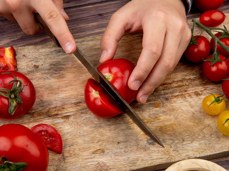 uomo taglia i pomodori freschi per mangiarli crudi