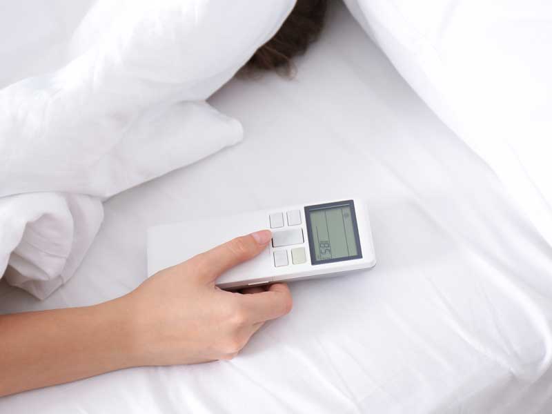 uomo a letto che tiene in mano il comando del climatizzatore