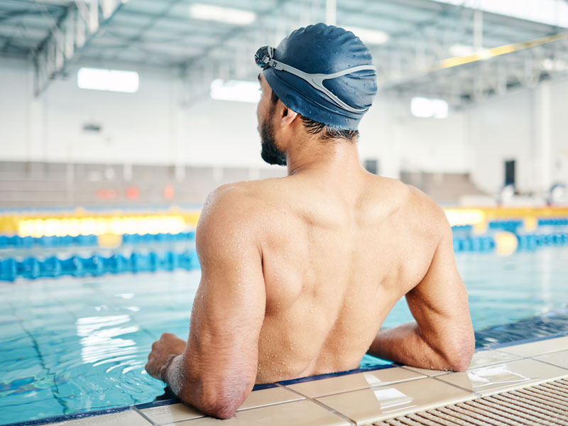 Uomo di schiena in piscina durante un allenamento di nuoto per migliorare la postura.